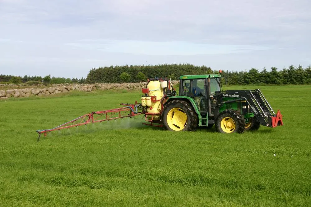 Traktor med sprøytebom i arbeid på norsk eng